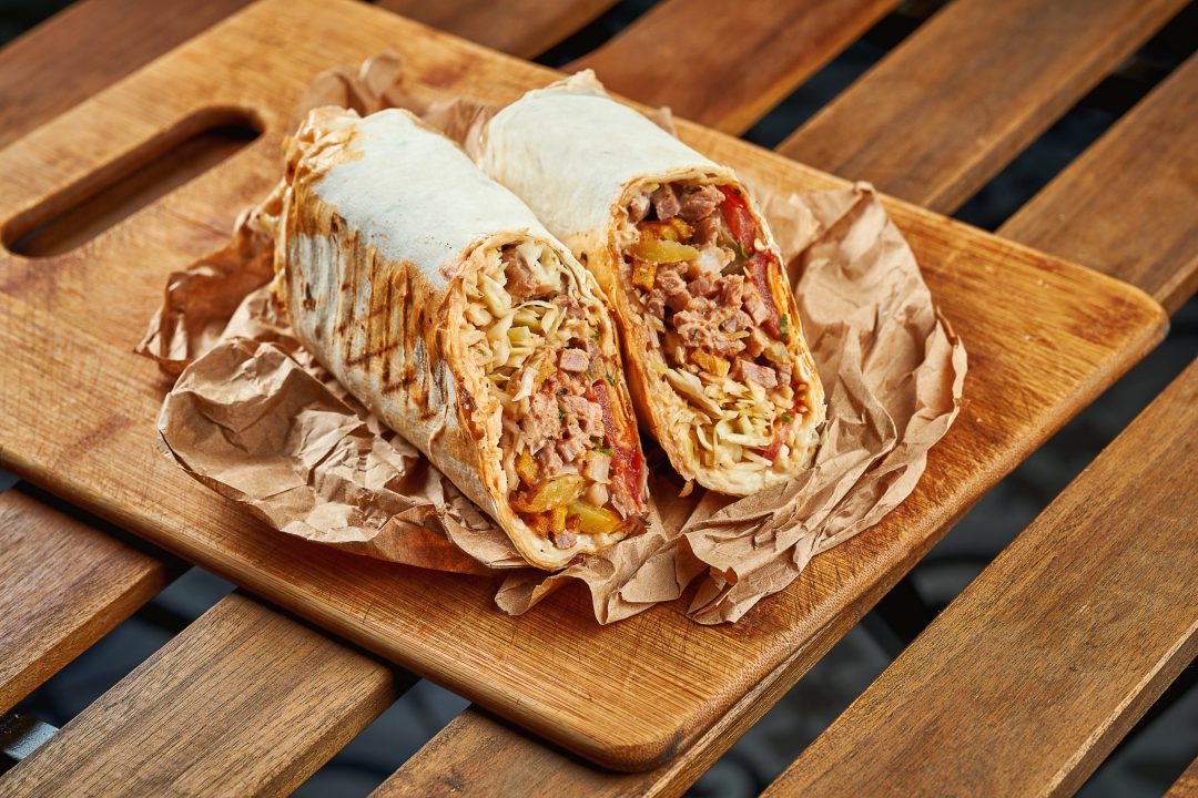 Large shawarma with meat and vegetables in kraft paper on a wooden background